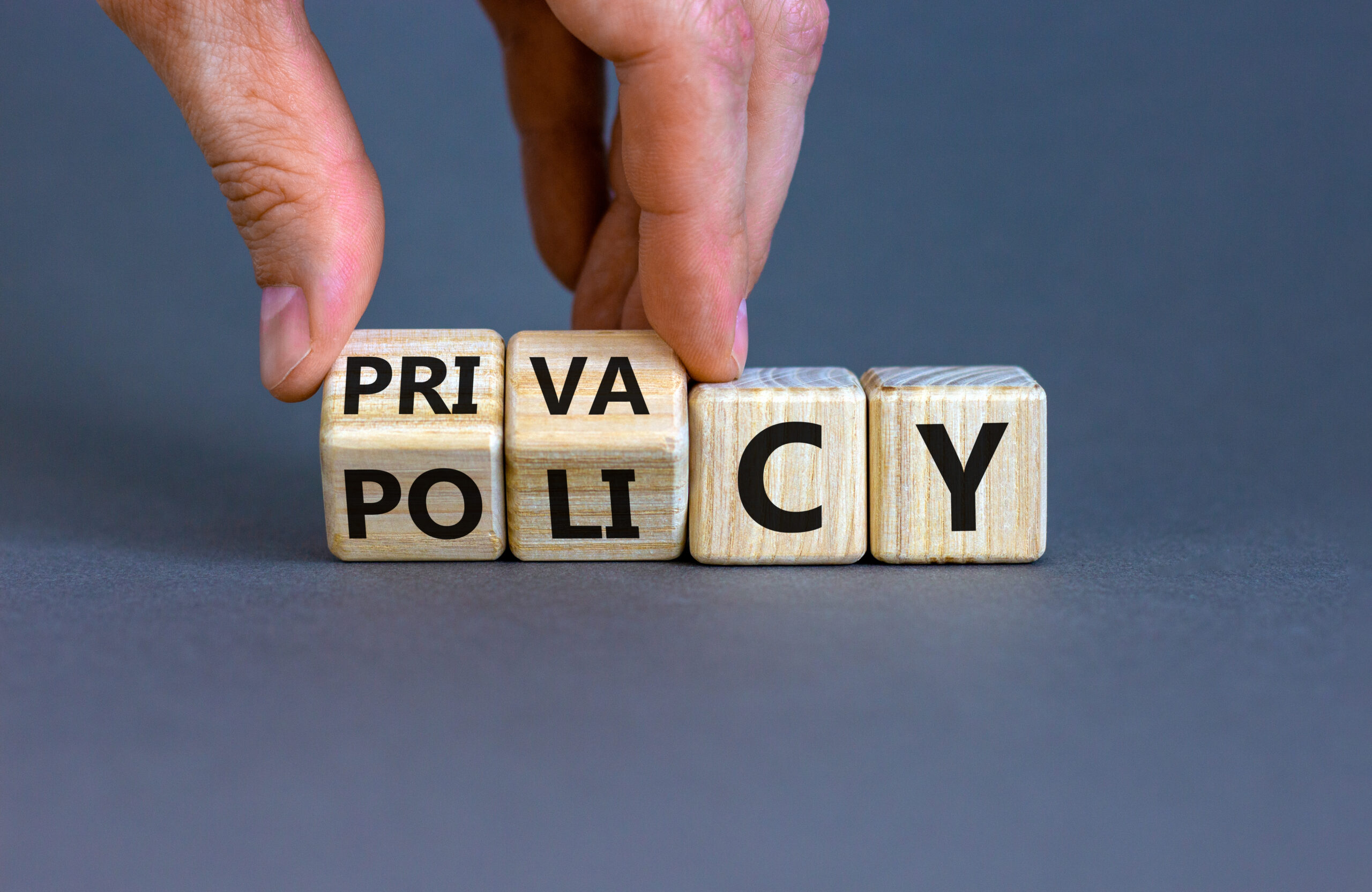 Privacy policy symbol. Hand turns the wooden cube with words 'Privacy policy' on a grey background.